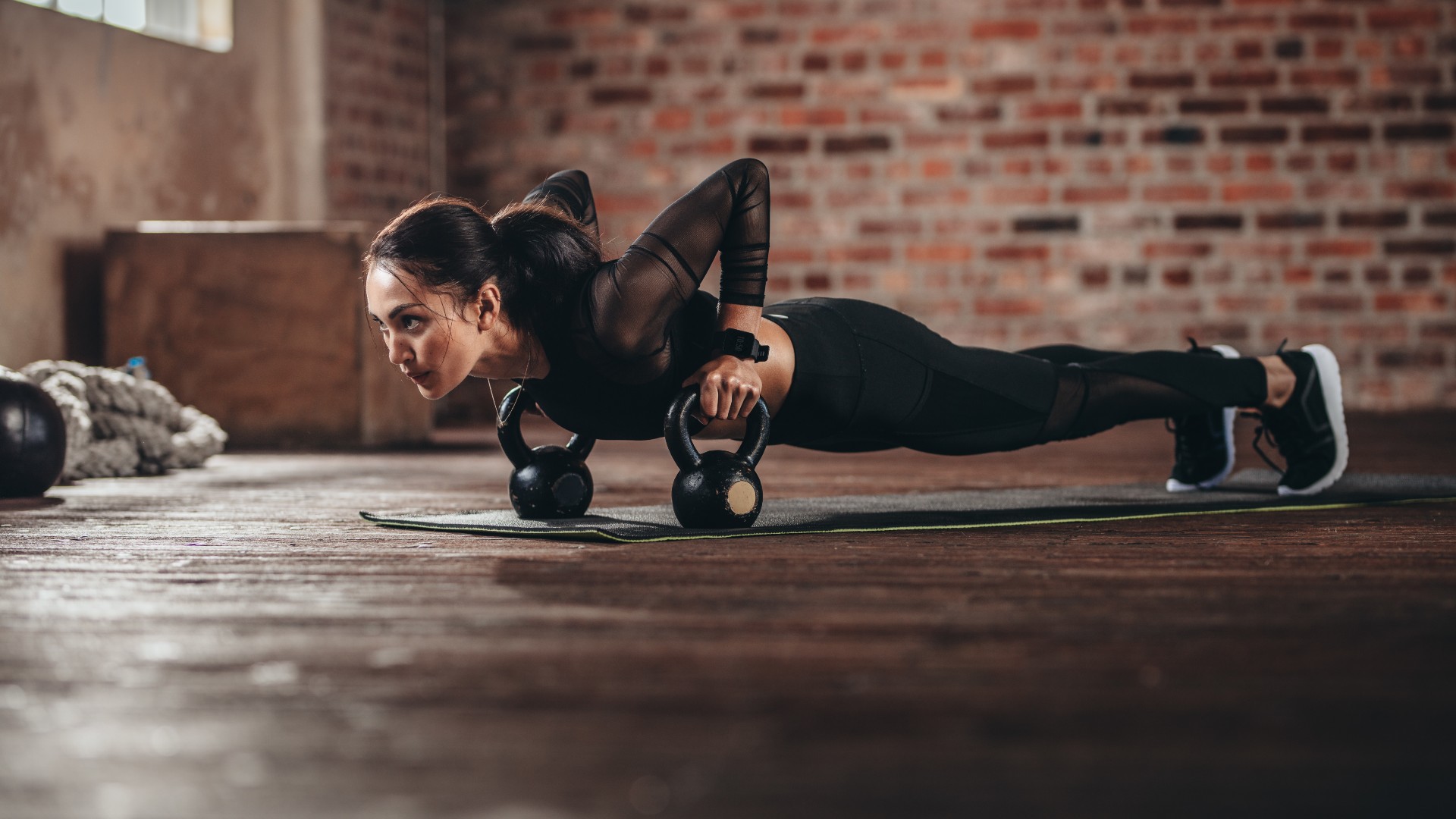 Woman performing a deficit negative push-up holding two kettlebells in her hands in a gym