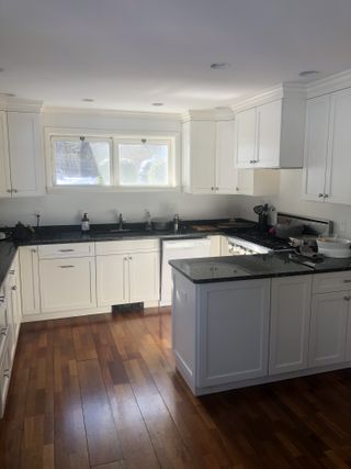 A dated kitchen with white cabinetry, wooden flooring, and dark granite worktops