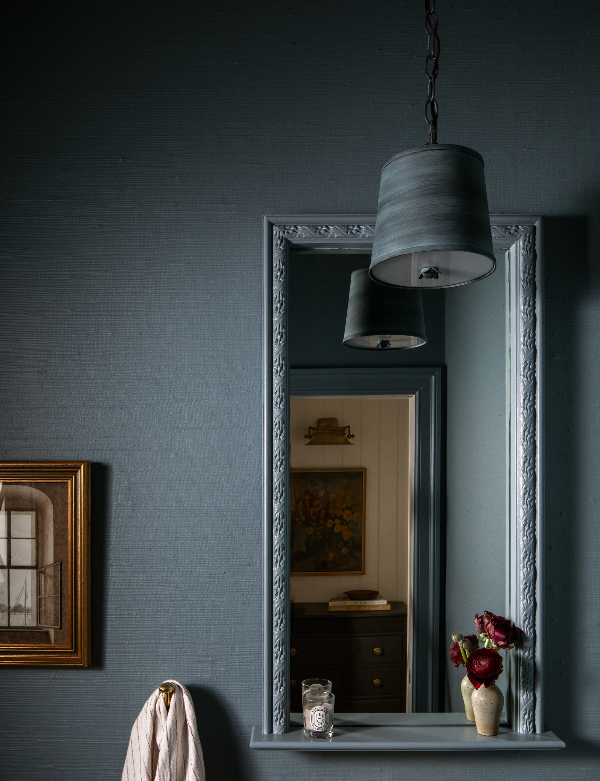 Blue-gray washed bathroom area featuring a pendant light, gold framed oil painting, and mirror