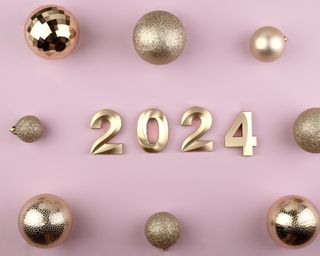 Golden symbols of 2024 on a pink background with Christmas balls