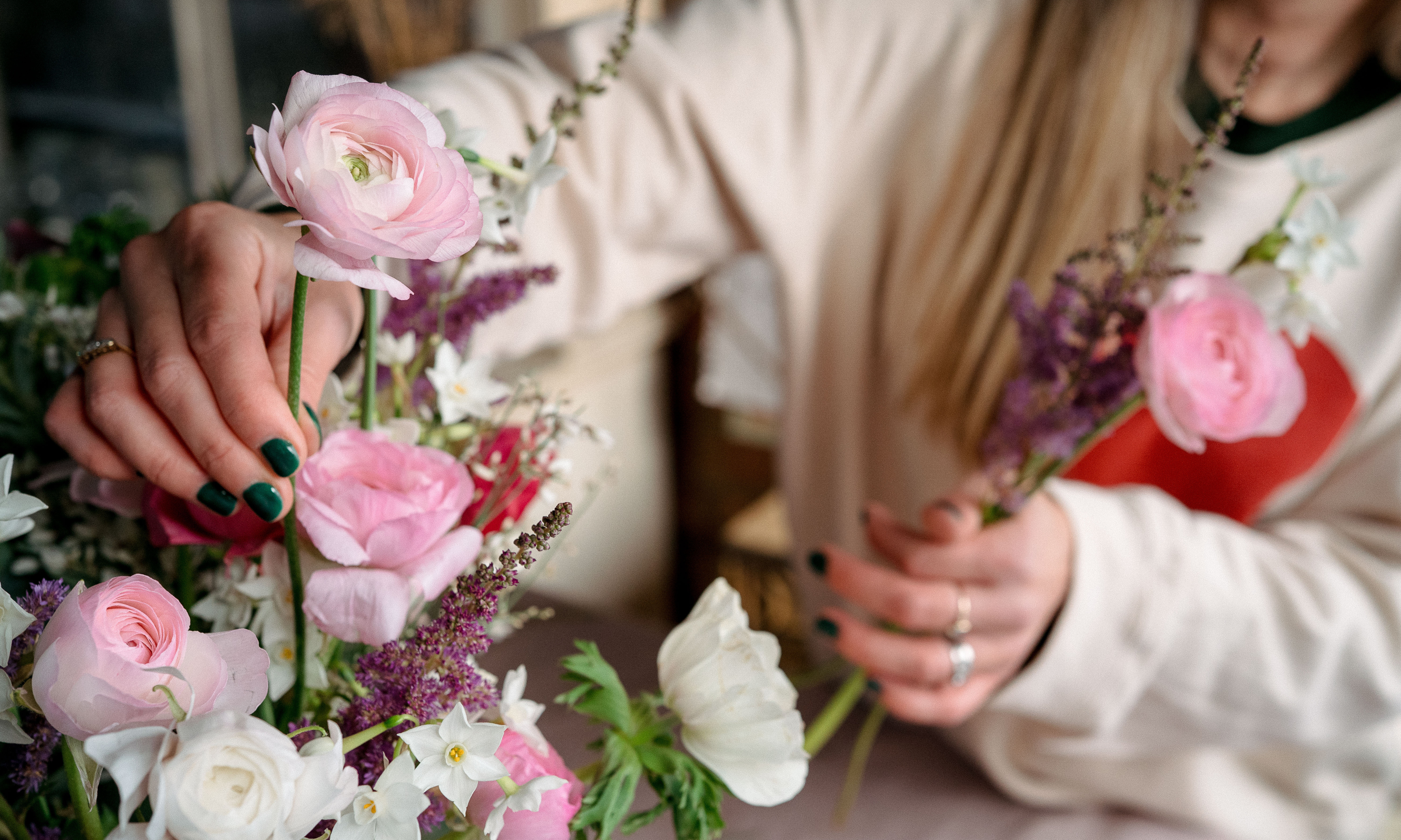 Hand placing pink ranunculus into an arrangement