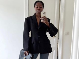 Influencer Sylvie Mus poses for a mirror selfie in a structured, cinch-waist black blazer, drop earrings, and jeans.