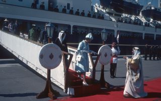 Queen Elizabeth climbing down the gangway of the Royal Yacht Britannia to meet men in white traditional headdresses in Bahrain