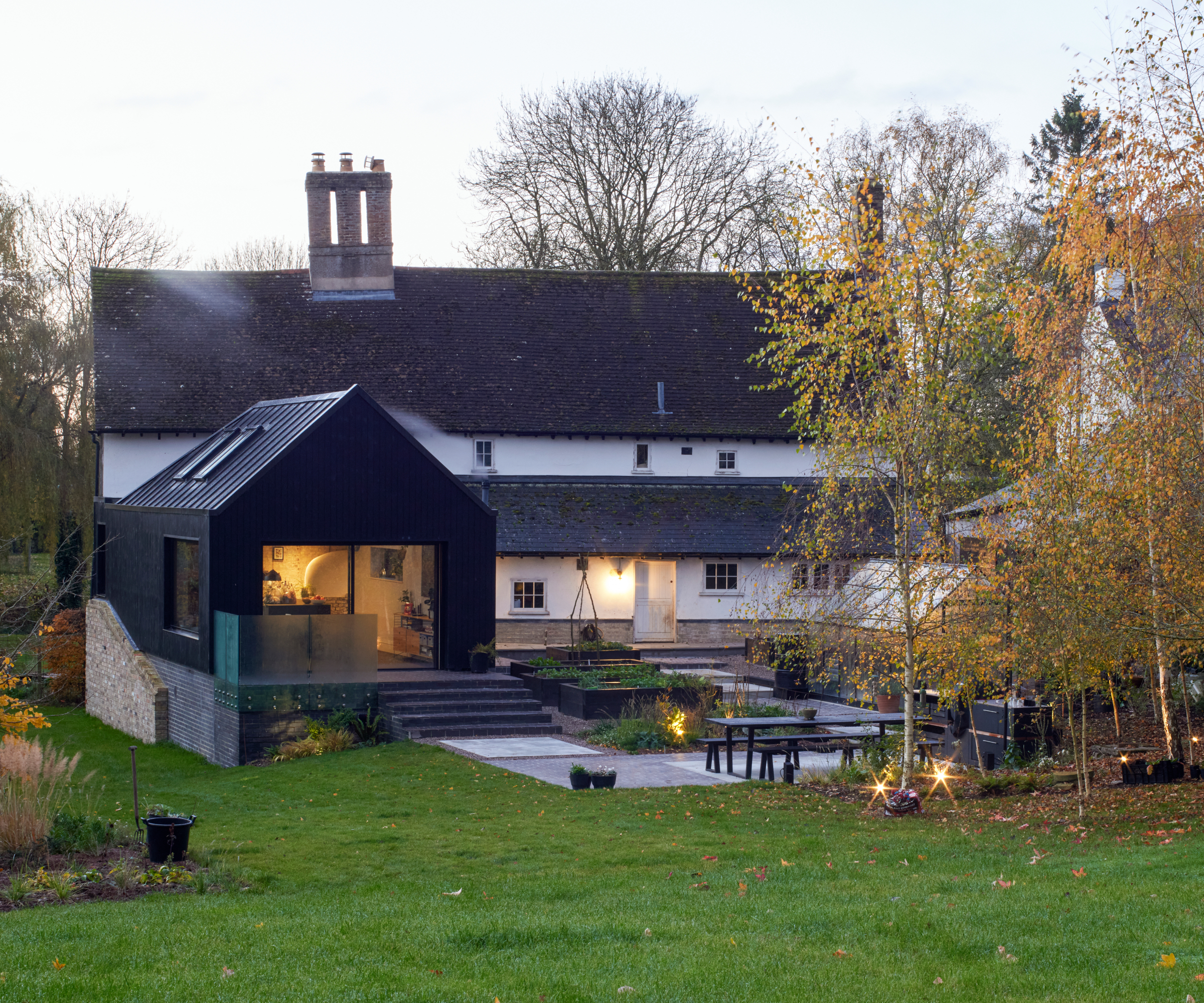 black clad pitched roof single storey rear extension with large patio doors at rear on large white and black slate tiled historic property in large gardens