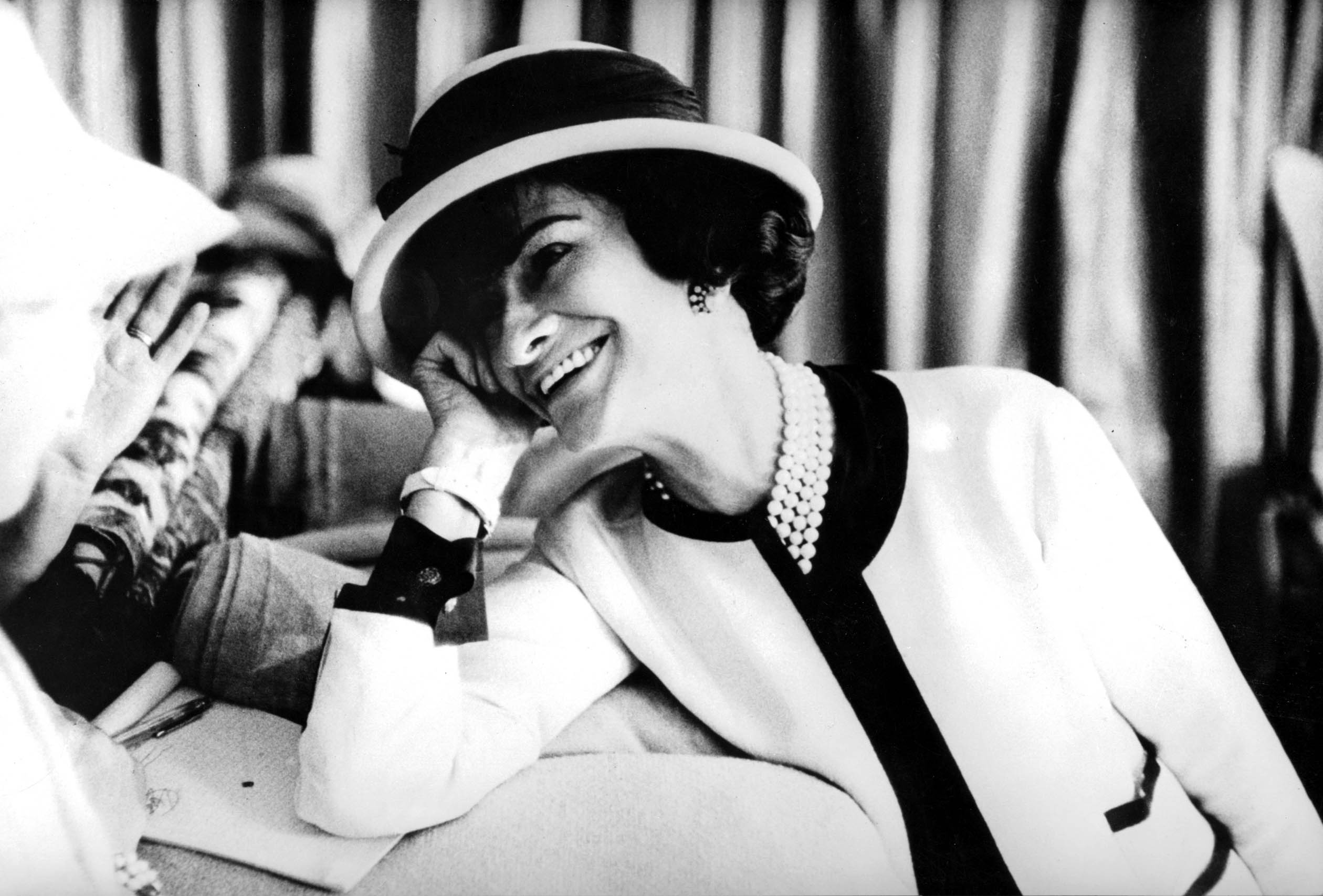 Gabrielle Chanel photographed in a white and black blazer, leaning on one arm