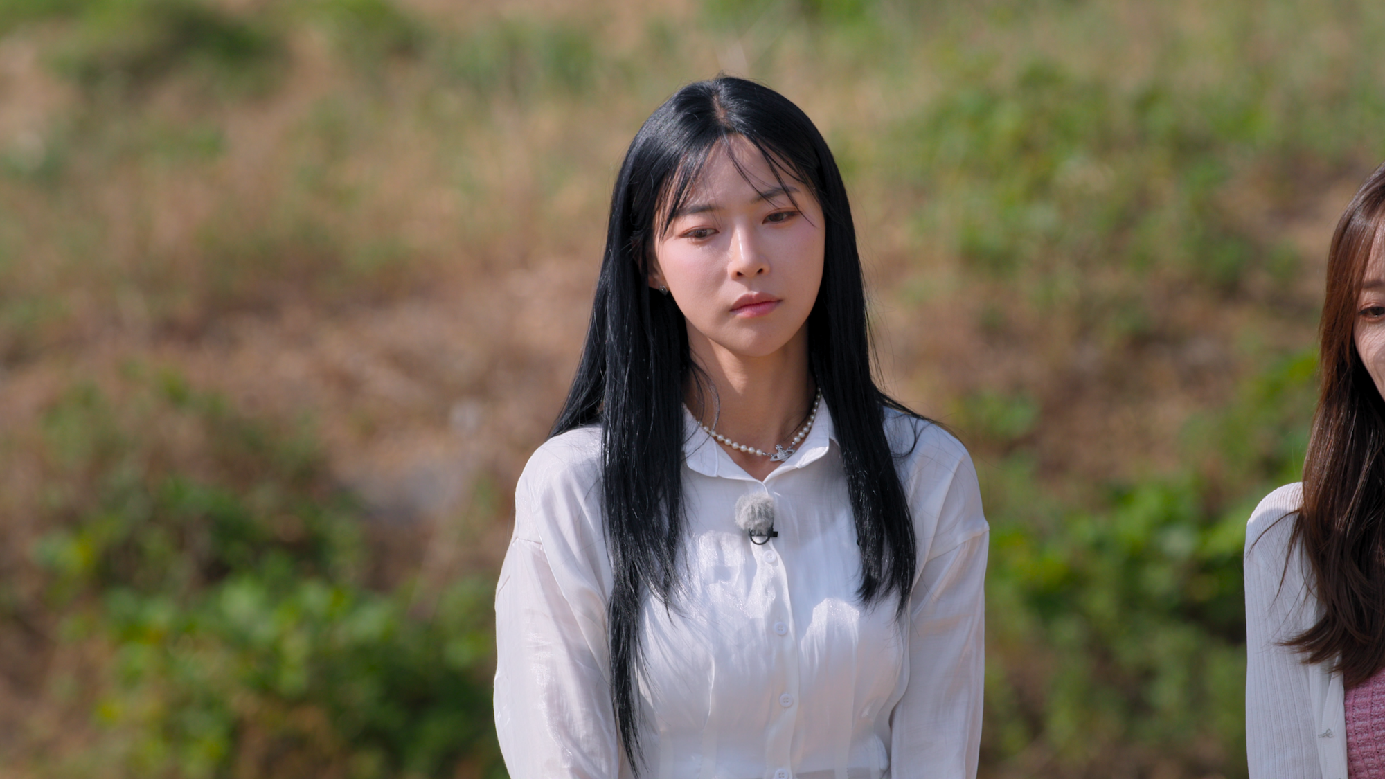 A Korean woman wearing white (Kim Min-gee) stands outdoors next to an unseen woman, in the Netflix Korean reality show 'Single's Inferno' season 5.
