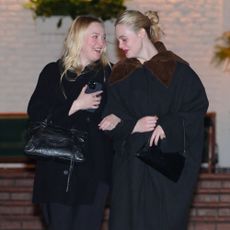 Ella and Dakota Fanning walk arm-in-arm wearing matching black outfits.