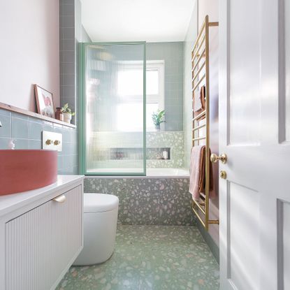 a small bathroom with green wall tiles, a bright coral modern bowl basin and green terrazzo walls and floor around a shower bath
