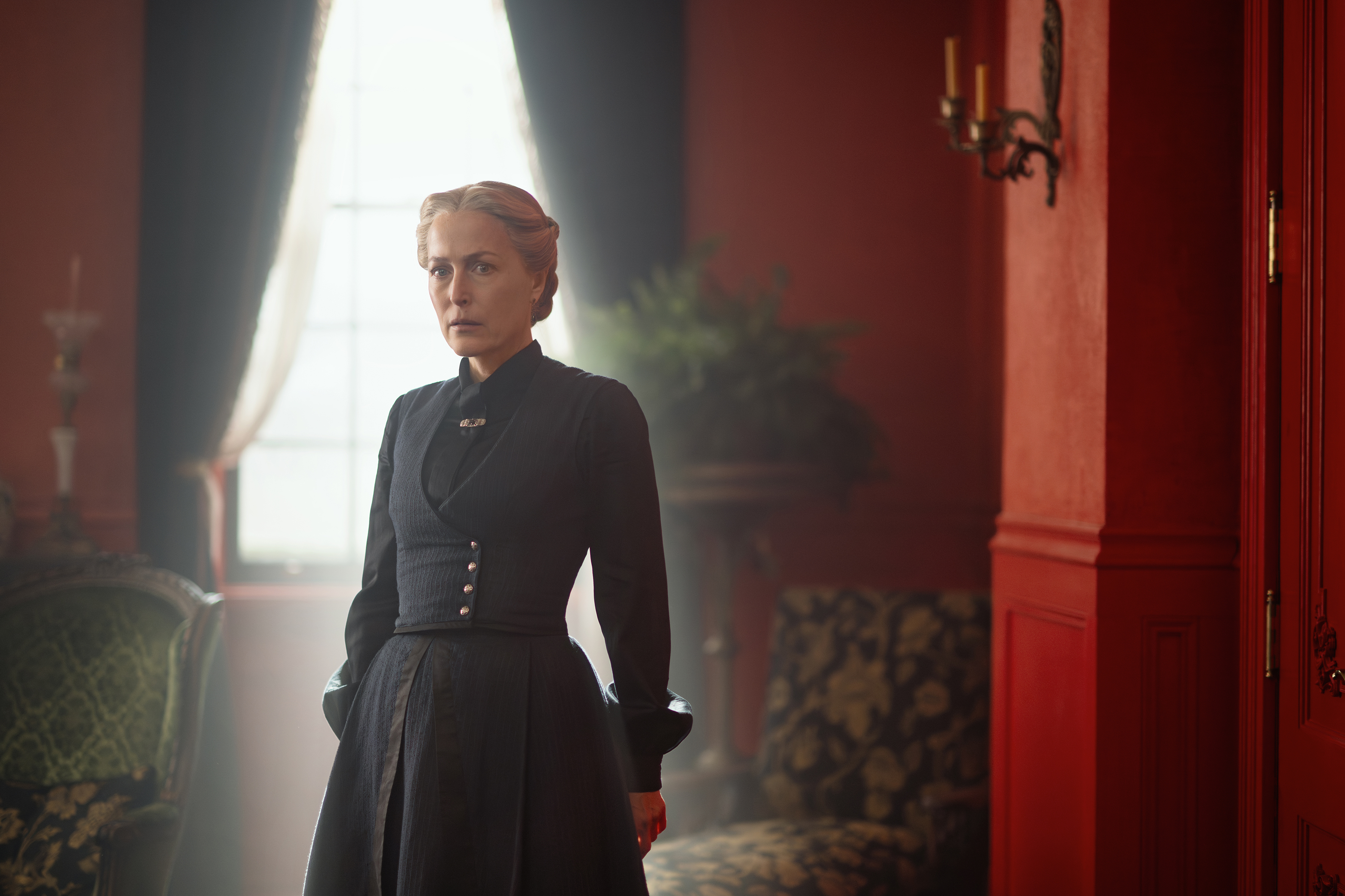 gillian anderson as constance van ness wearing a black dress and standing in a parlor looking worried in the abandons