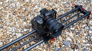 Neewer ER1 Motorized Carbon Fiber Camera Slider with a Sony camera attached outside on a stony ground