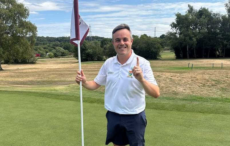 A golfer holds up their finger and the flag after a hole-in-one