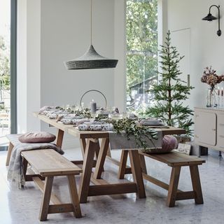 A dining room with a long rectangular table set for Christmas and two dining benches with a Christmas tree in the background