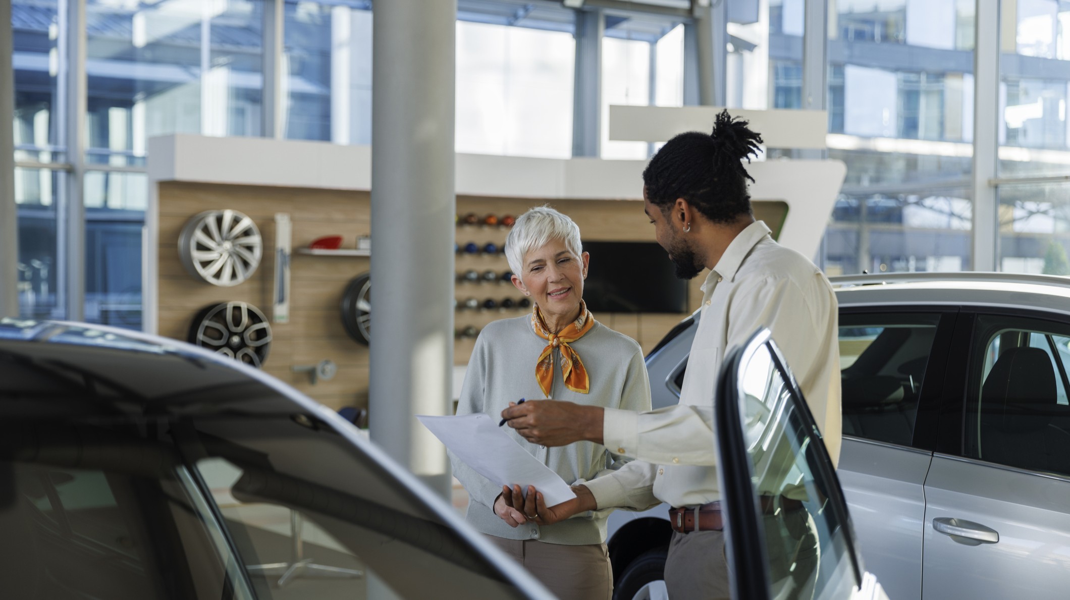 A car salesman presents a contract to a mature woman inside a dealership. 
