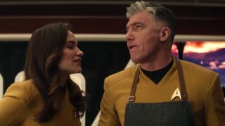 two people in gold starfleet uniforms smile at one another