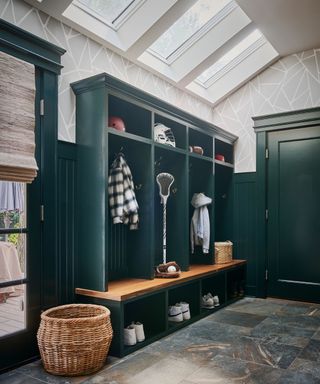 A mudroom with dark green built-in shelves, marble floors, and three large skylights