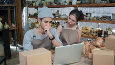A business owner and his partner look stressed as they look at a laptop in their ceramics shop. 