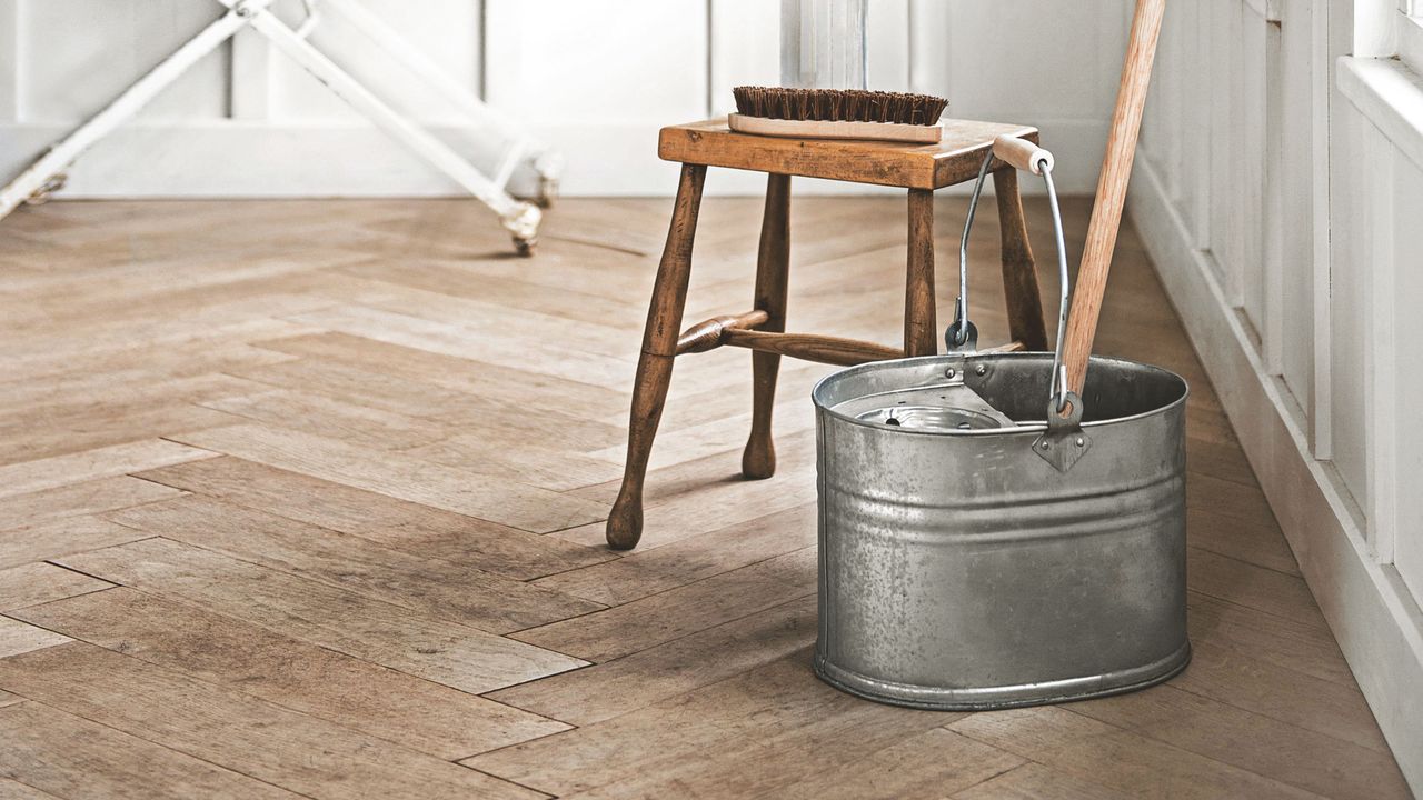 Wooden floor with a metal bucket and mop sitting on it, next to a wooden stool