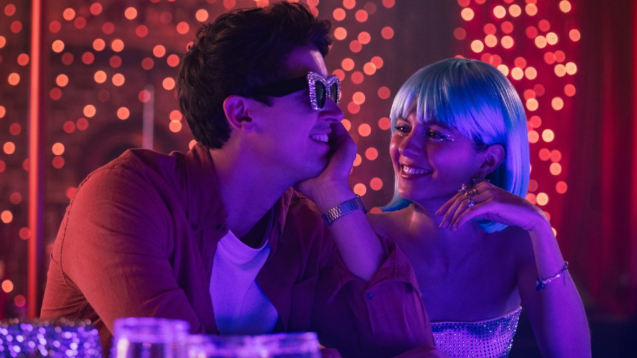 From left to right: Alex wearing fun sunglasses while Poppy looks at him lovingly while wearing a blue wig. 