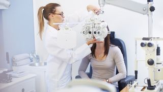 A woman with dark hair has her eyes tested by an optician