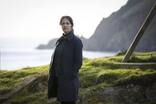 Shetland season 8 will feature DS Alison 'Tosh' Mackintosh (Alison O'Donnell) who is standing on a grassy clifftop, looking toward the camera with her body turned to the left of the frame. She is wearing a long dark coat over a rollneck top and trousers.
