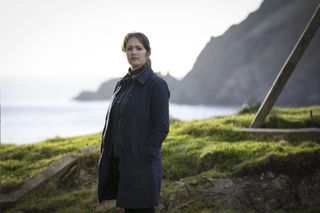 Shetland&#039;s DS Alison &#039;Tosh&#039; Mackintosh (Alison O&#039;Donnell) stands on a grassy clifftop, looking toward the camera with her body turned to the left of the frame. She is wearing a long dark coat over a rollneck top and trousers.