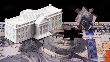a small 3d rendition of the White House on top of a puzzle of the one-hundred dollar bill with one puzzle piece taken out of the puzzle