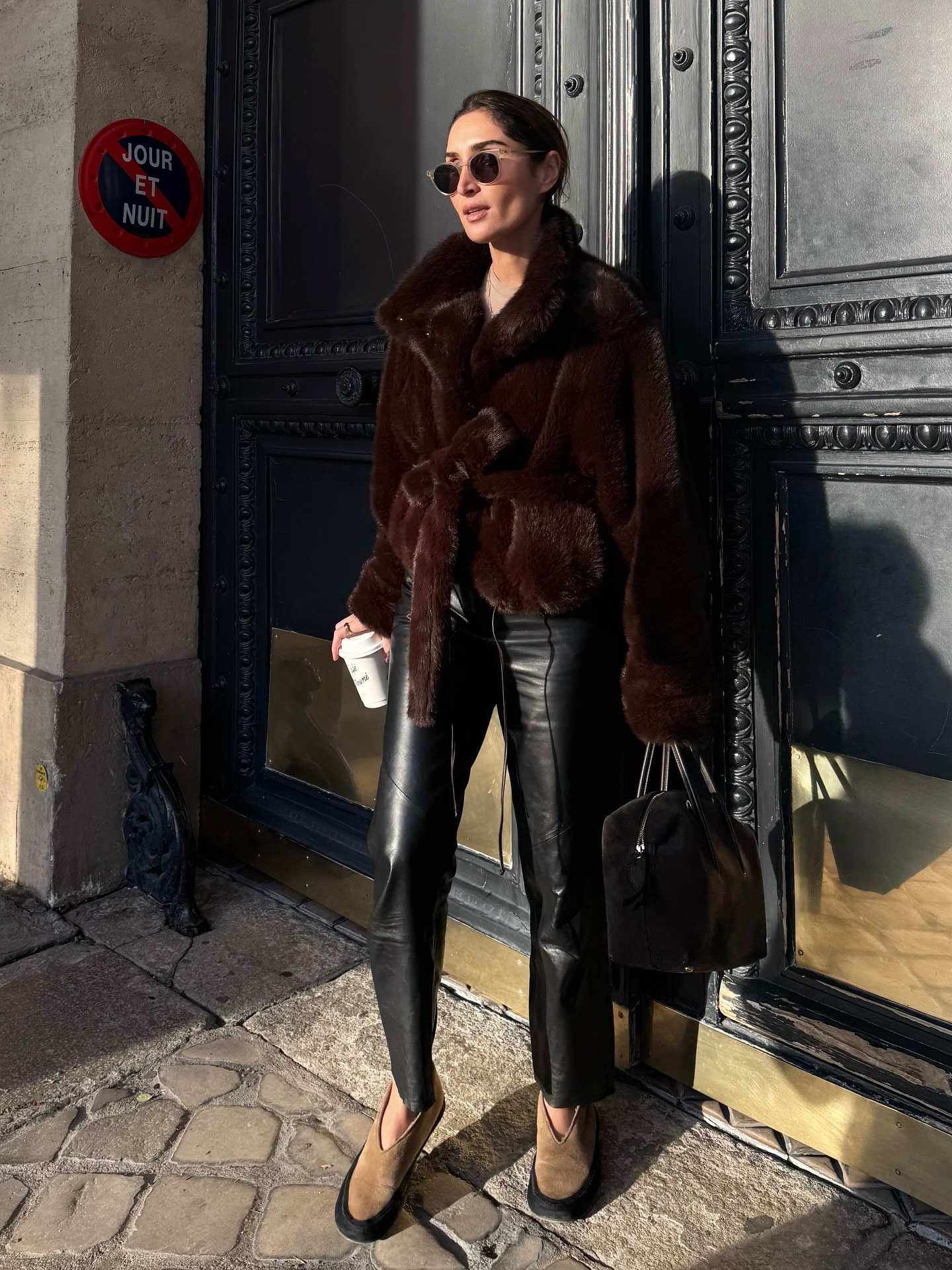 Erin wears a brown fur coat, black leather pants, a black bag, and beige flats.