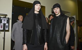 Two male models wearing black outfits and head wear