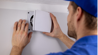 man taking the cover off an extractor fan on the wall