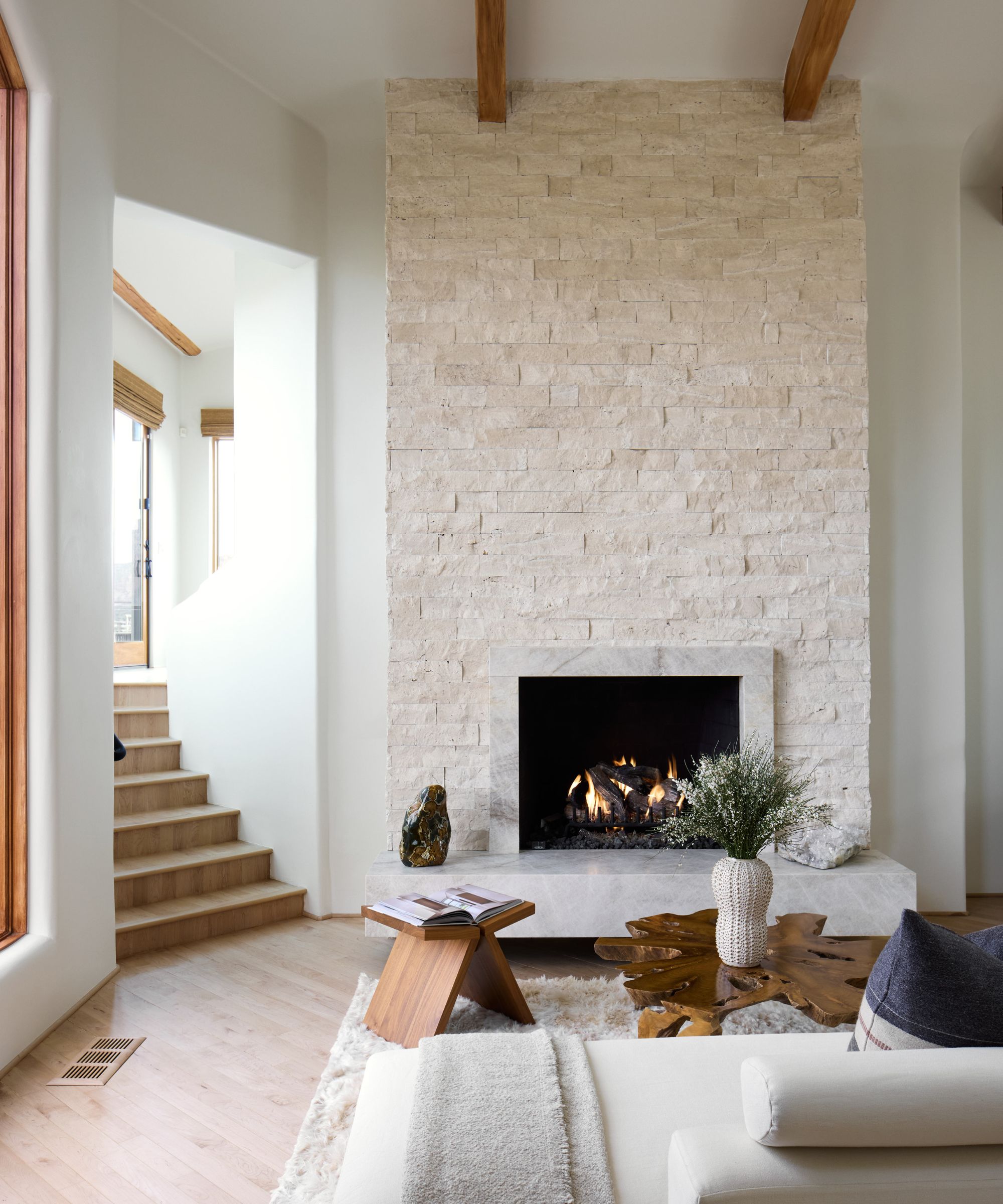 Modern neutral living roon with large white brick fireplace, light wood floor, wooden tables, cream sofa with throw and pillows