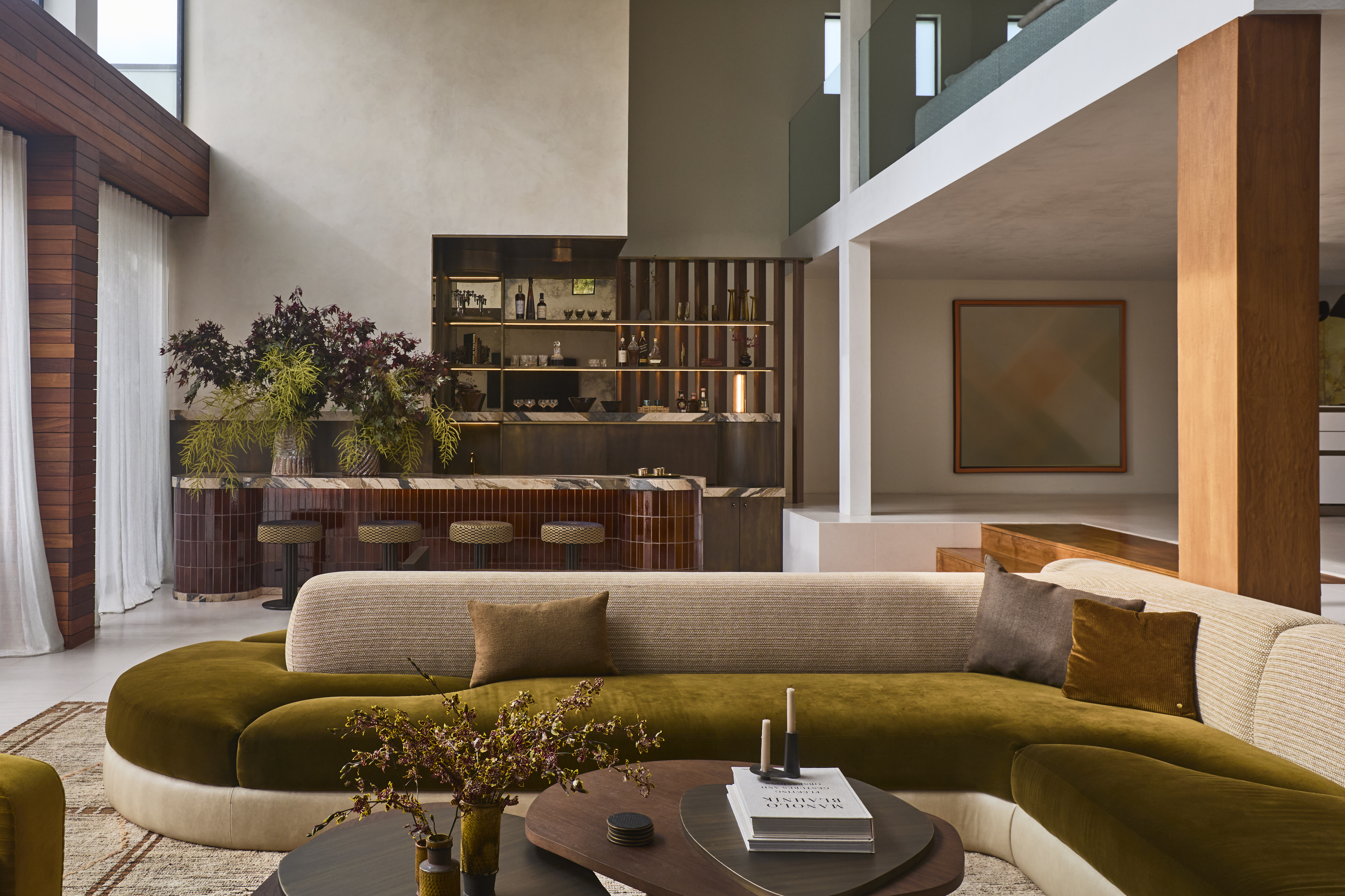 A modern open plan living space with a modern sofa and home bar with a nesting coffee table design styled with flowers candles and books