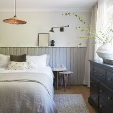 Light coloured bedroom with cushioned wall panelling, grey throw and cushions on bed with hanging light
