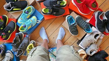 Man deciding what to wear surrounded by various trainers and casual footwear