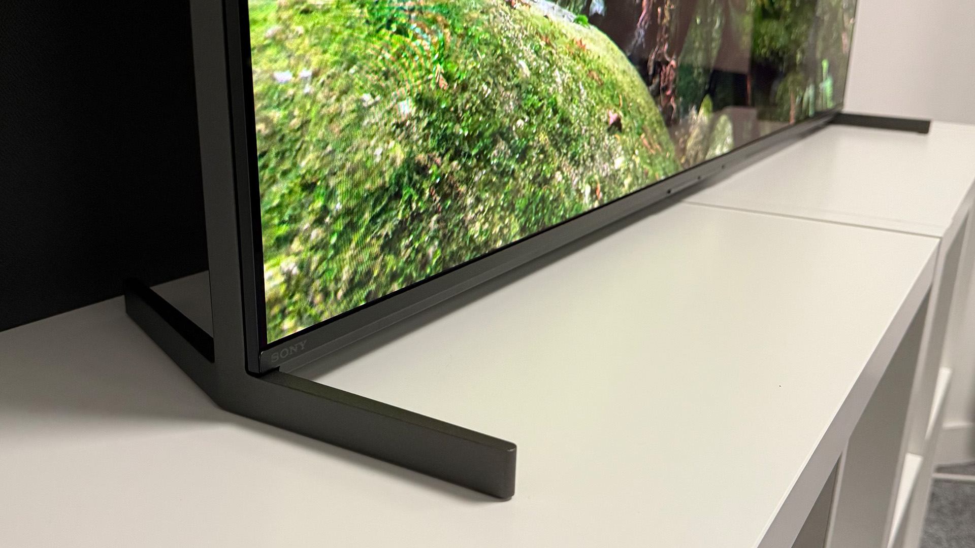 Close-up of the stand on the 55-inch Sony Bravia 8 II QD-OLED TV photographed on a white table. On the screen is a nature documentary.