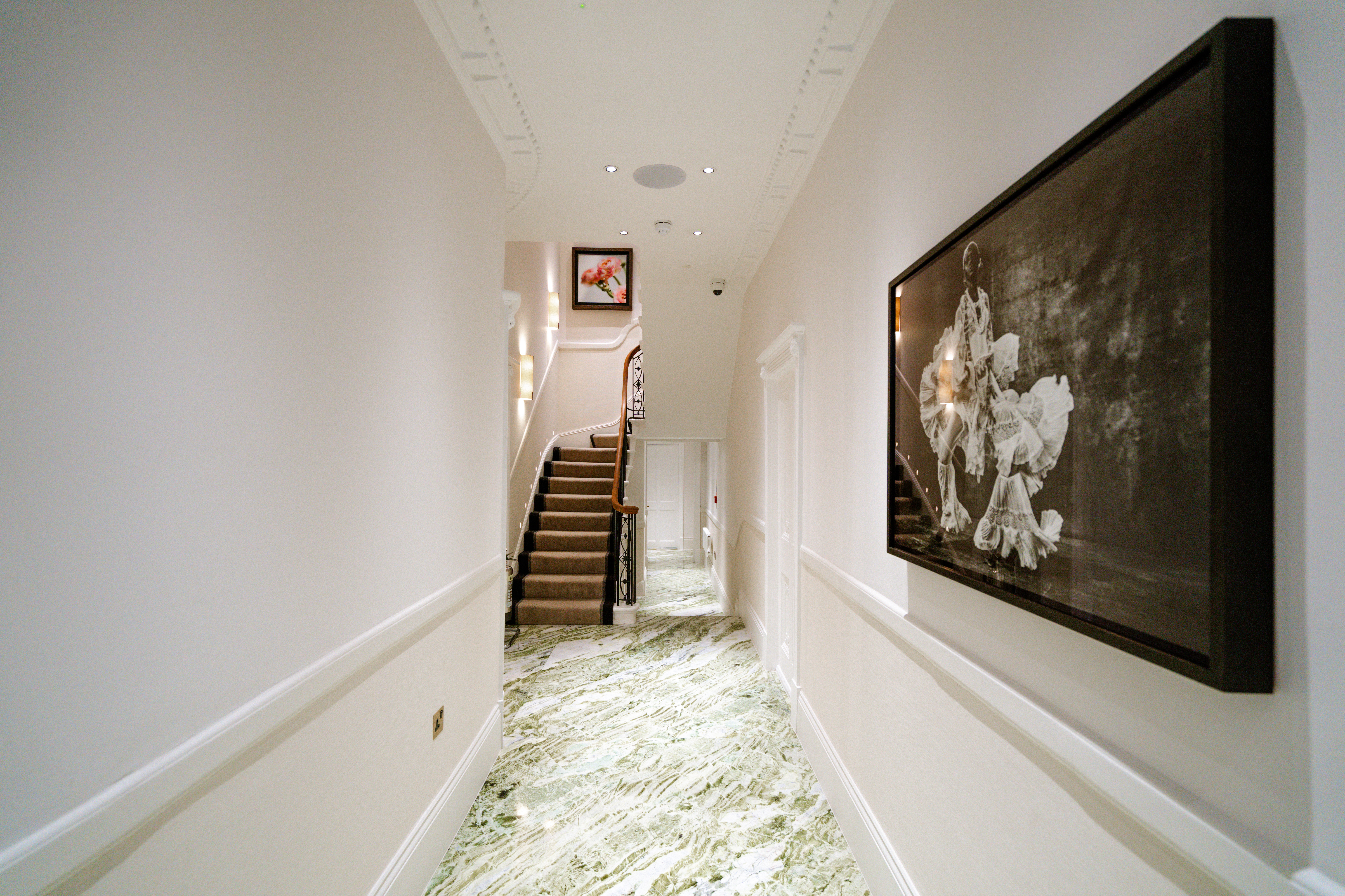 The entrance hallway of a beauty salon is decorated with shiny green and white marble, a large-scale, framed monochromatic portrait of a dancer in an ornate, voluminous dress, and wrought iron and wood details.