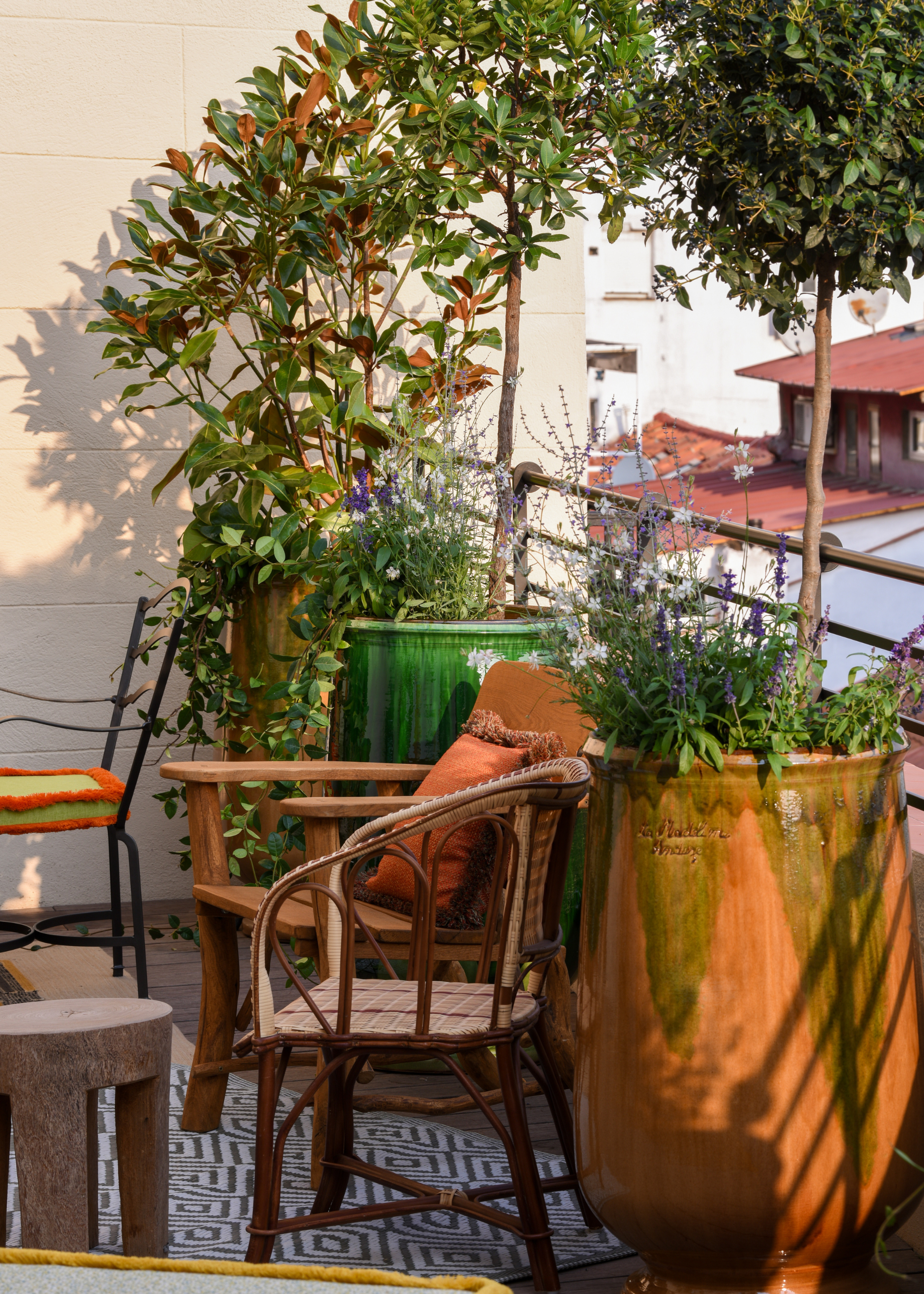 An outdoor balcony space connected to a hotel room with organic furniture and large potted trees