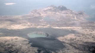 View of Ukinrek Maars in Alaska. We see a crater filled with water and a lake in the distance.