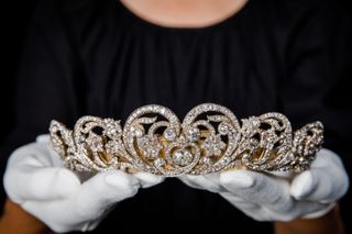 A person in a black top wearing white gloves holding the Spencer diamond tiara in their hands