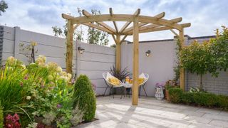 wooden corner pergola in patio area with two yellow chairs 