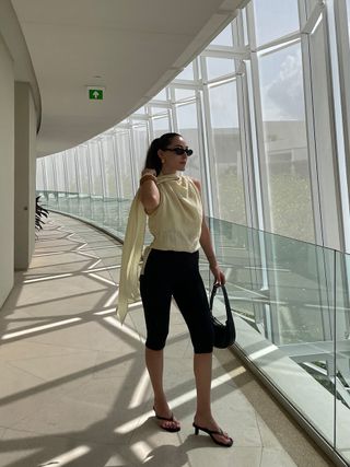 Anna LaPlaca trug ein Zara-Schaloberteil, schwarze Capri-Leggings, hochhackige Zehensandalen und goldene Heaven Mayhem-Ohrringe