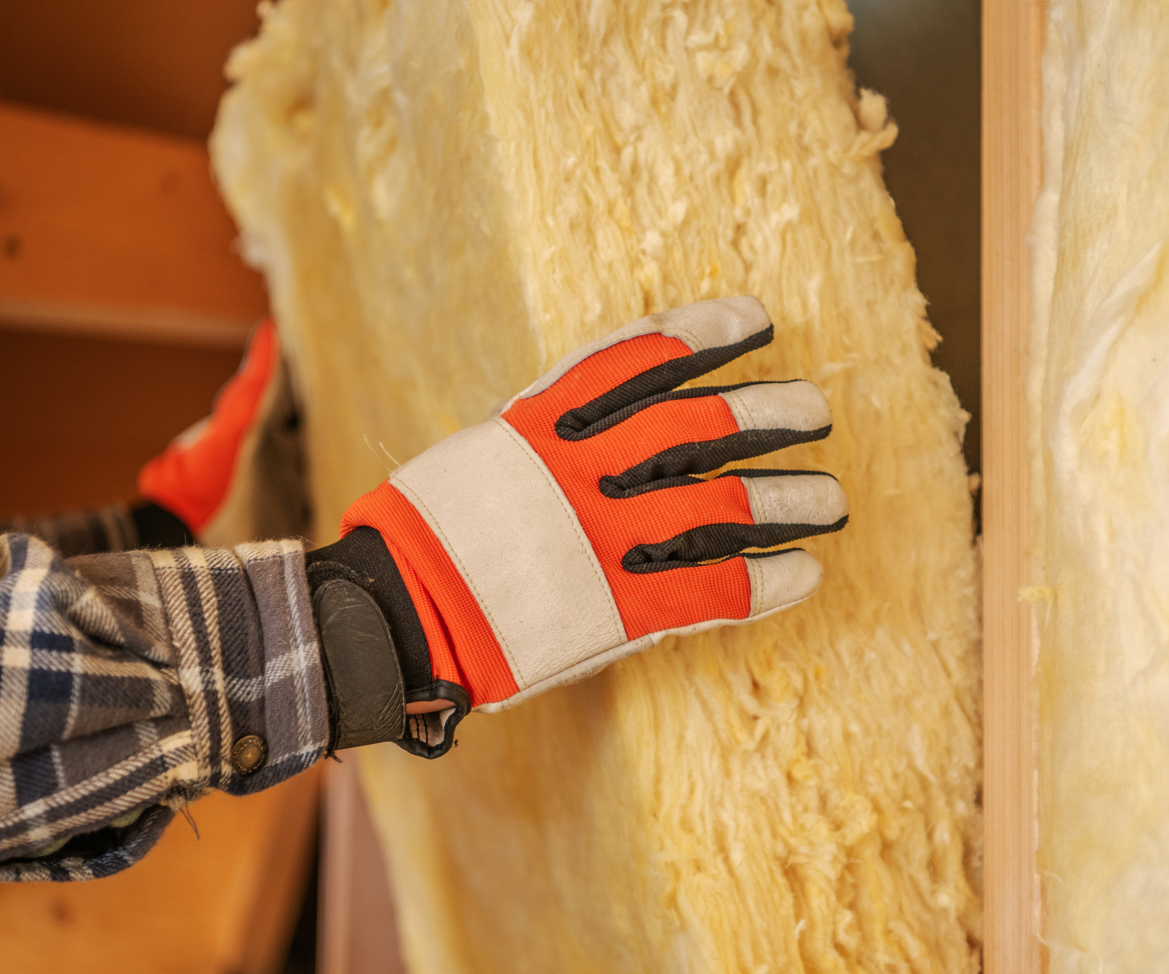 Gloved hands placing internal insulation inside a wall