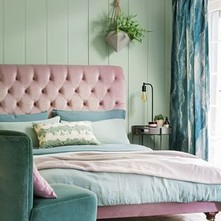 Green bedroom with armchair, hanging plant and bed with pink headboard