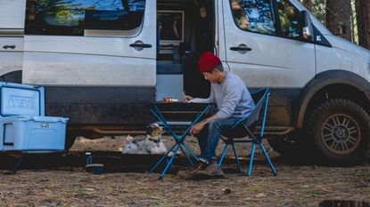 best camping table: man in front of campervan, eating from Helinox Cafe table