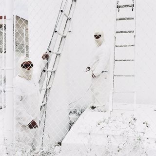 People in white safety suits next to a ladder on a white wall