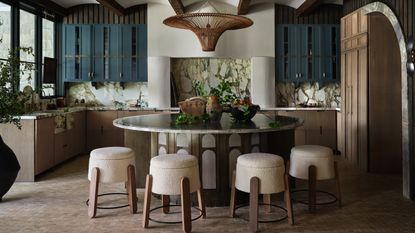 A modern kitchen with circular dining table, boucle bar stools, and small-format tile flooring in a warm grey tone