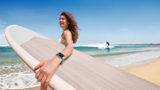 Image depicts a women on the beach wearing fitness gear, carrying a surfboard and the new Huawei FIT 3 watch