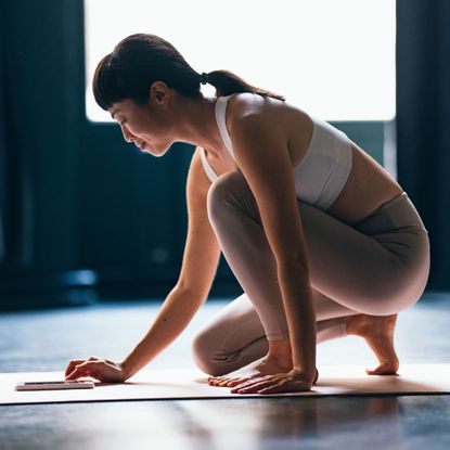 A woman in pink and white gym gear on a yoga mat, ready to do a Pilates workout