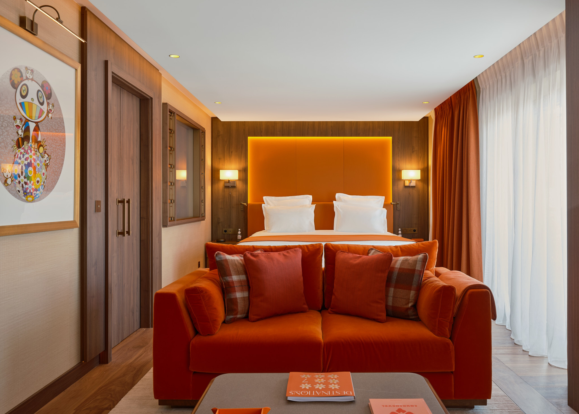One of the suites at Maya Hotel Courchevel 1850 with red details including a backlit red accent wall behind the bed, a red sofa in front of the bed and red curtains and wood flooring and paneling