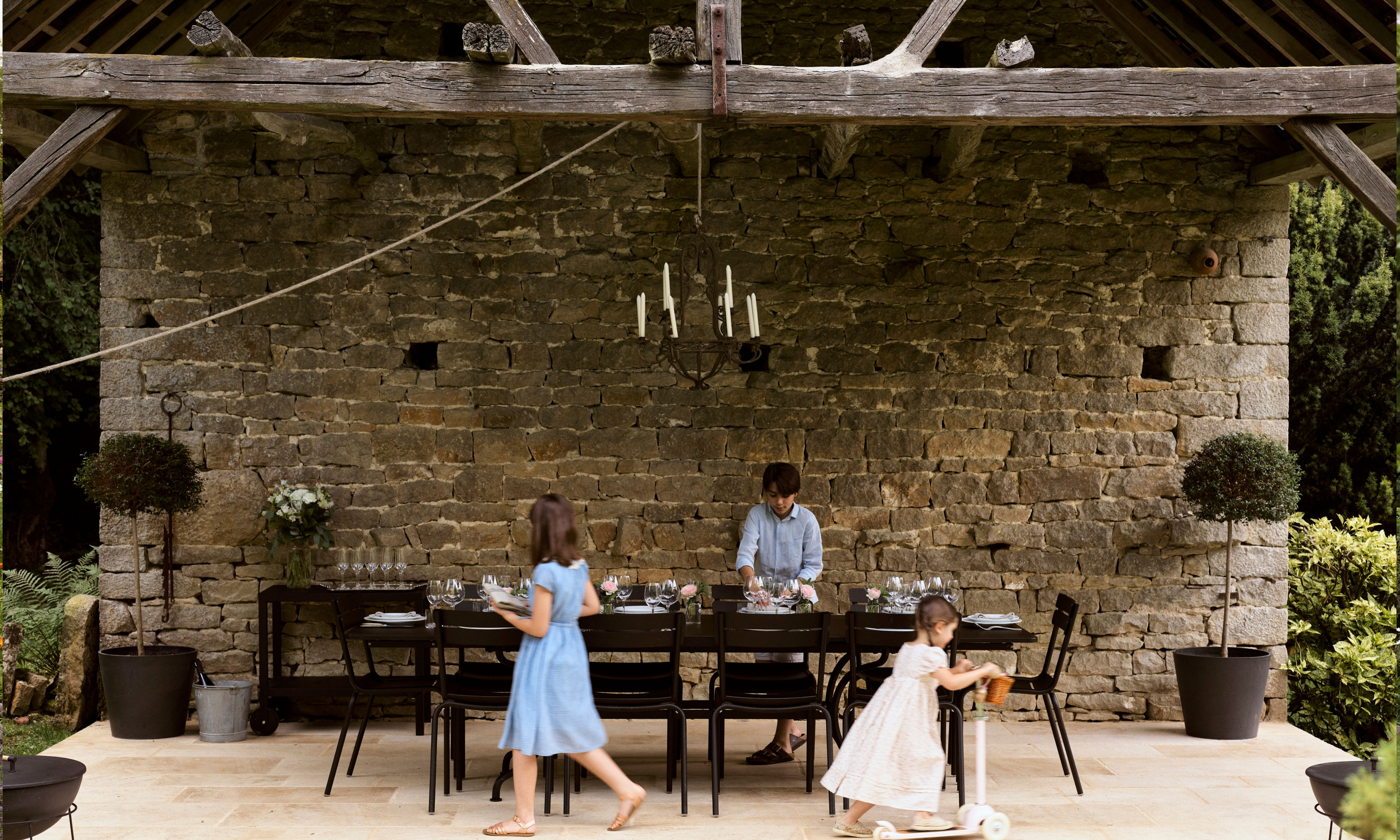 Children in an open stone barn setting a long banqueting table for dinner