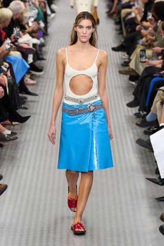 Ein Model trägt einen creme-weißen, ausgeschnittenen Badeanzug und einen strahlend blauen Midirock aus Lackleder auf der Miu Miu-Modenschau Frühjahr/Sommer 2025 in Paris.